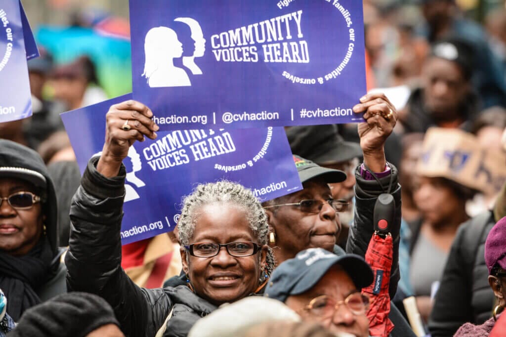 Picture of a woman in a crowd holding up a purple sign saying "Community Voices Heard"