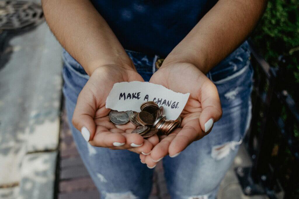 Photo of two hands holding coins and a paper saying, "Make a change."